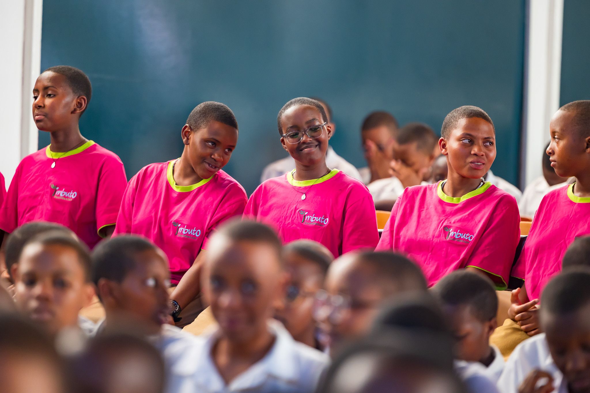 Students in pink T-shirts watch the ceremony from their seats