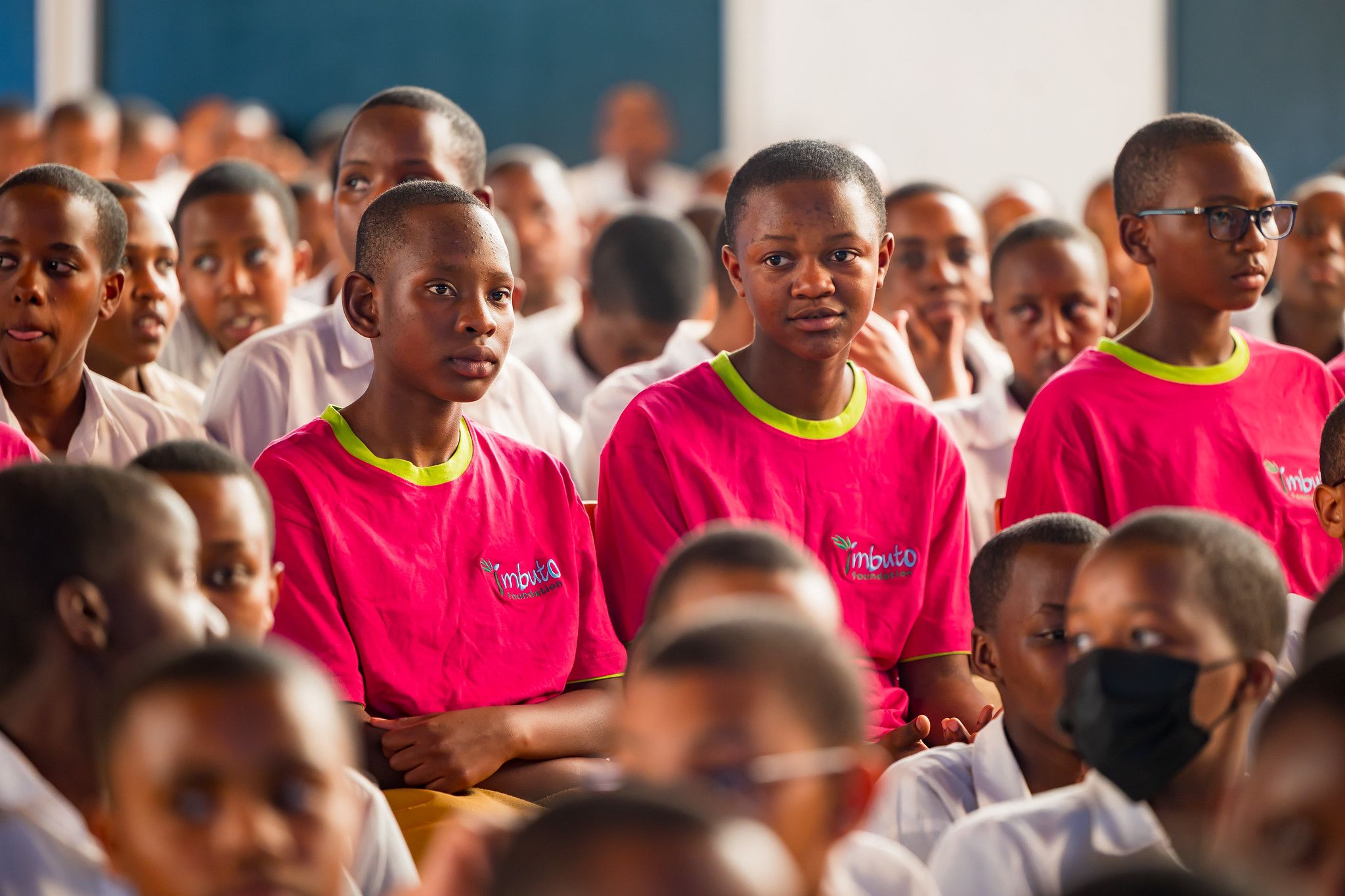 Students in pink Imbuto Foundation T-shirts seated together in the hall