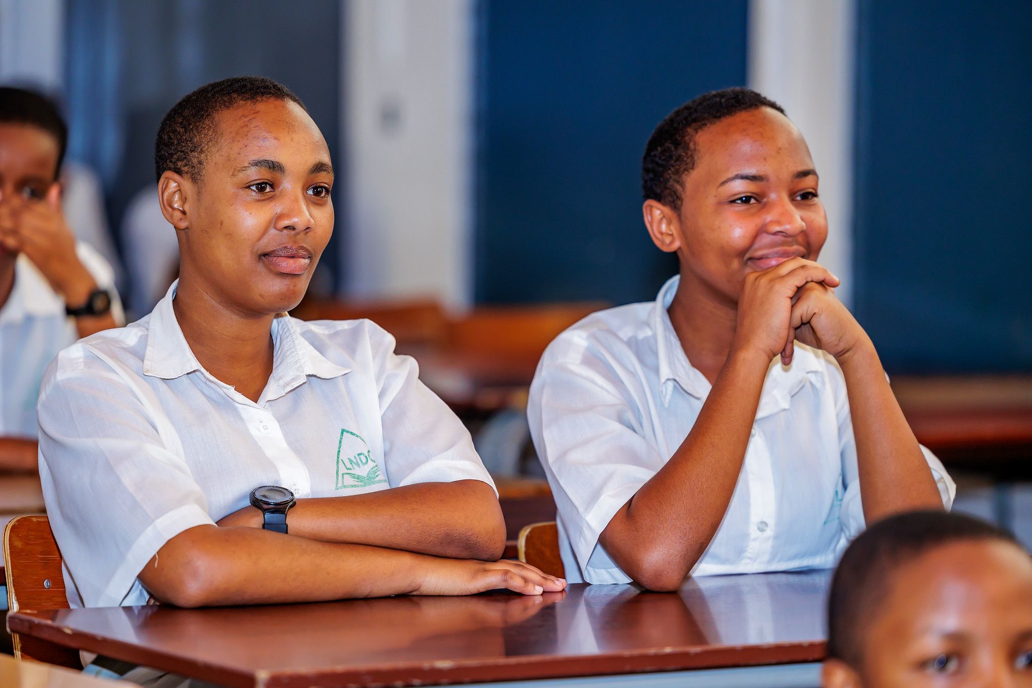 Two students sit side by side, one smiling with her chin on her hands