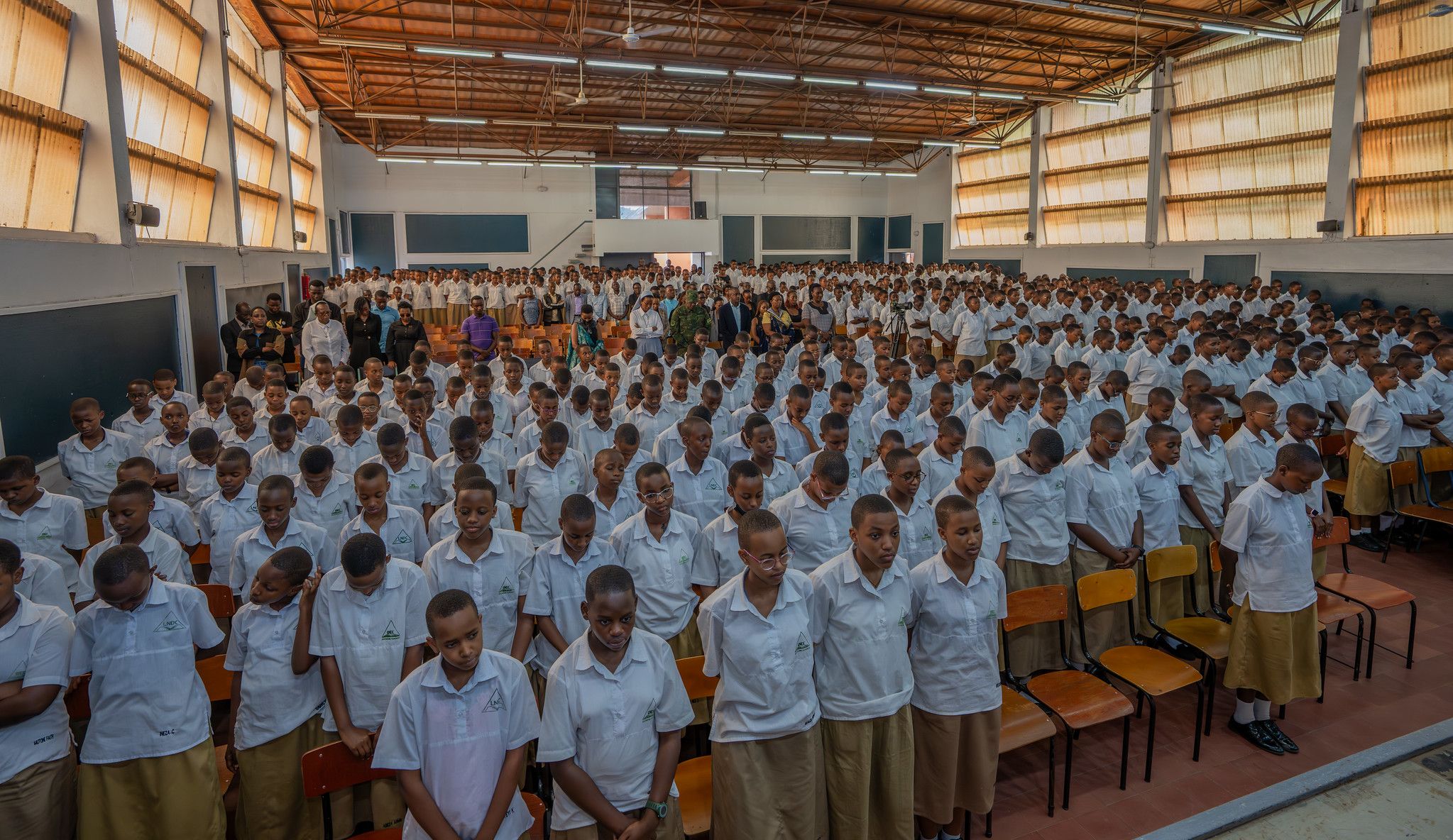 Hundreds of students stand with heads bowed in the Great Hall