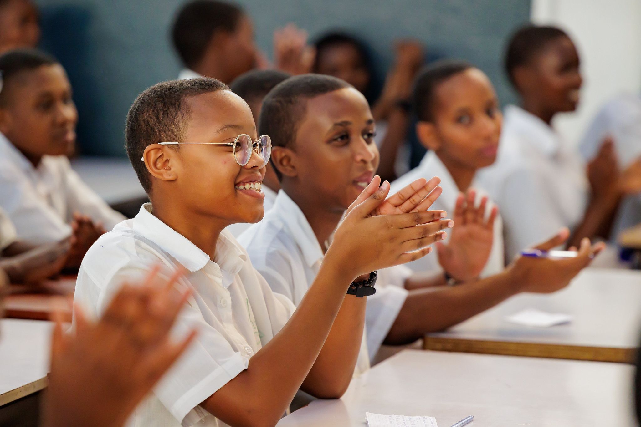 A student in round glasses laughs and claps with her classmates